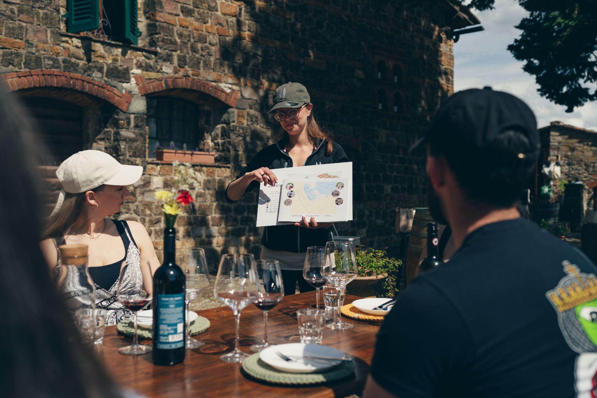 A Your Vino guide showing a vineyard map to guests at an outdoor tasting table in a Tuscan stone courtyard