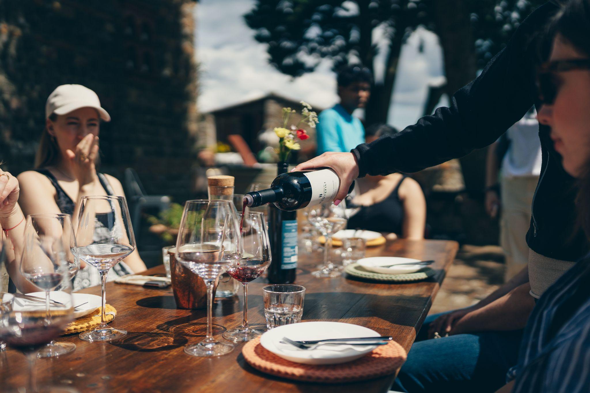 Red Tuscan wine being poured into glasses at an outdoor tasting table