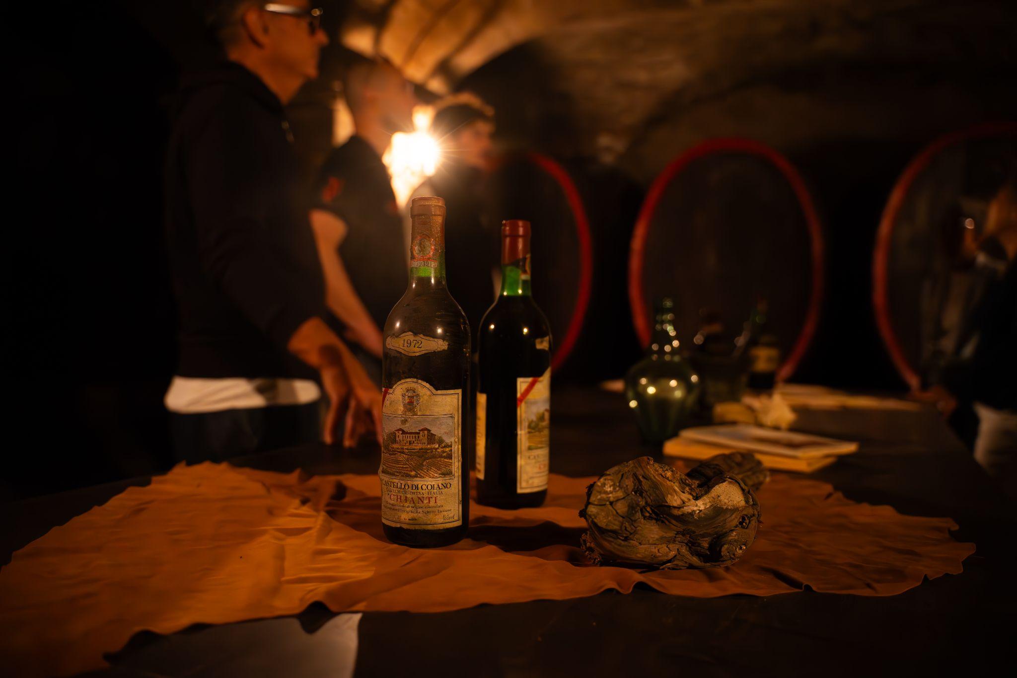 Aged bottles and an old vine root lit by candlelight in a historic Tuscan cellar with large barrels