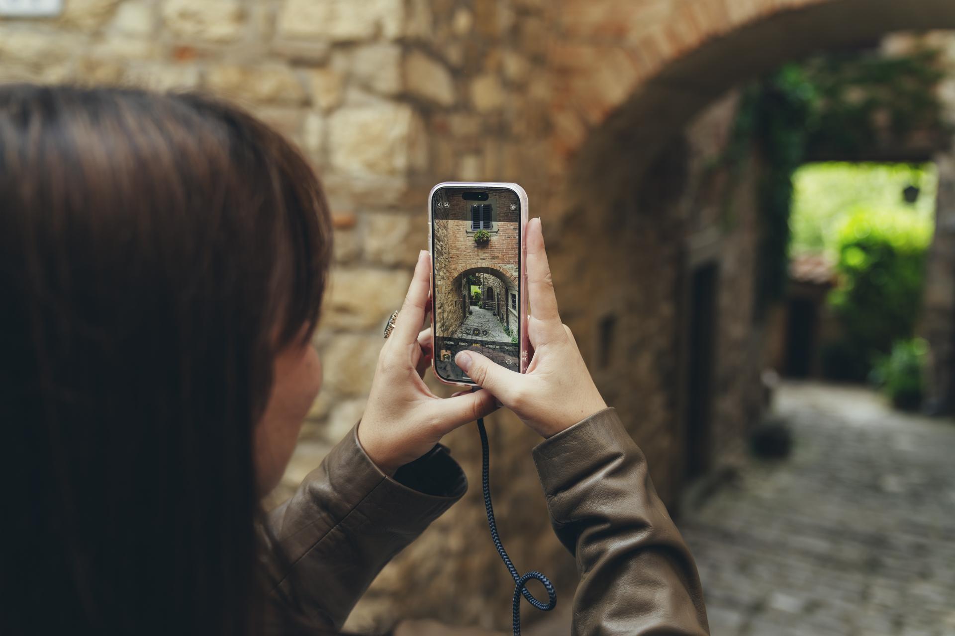 A visitor photographing a stone archway and cobbled alley in a Tuscan hill town