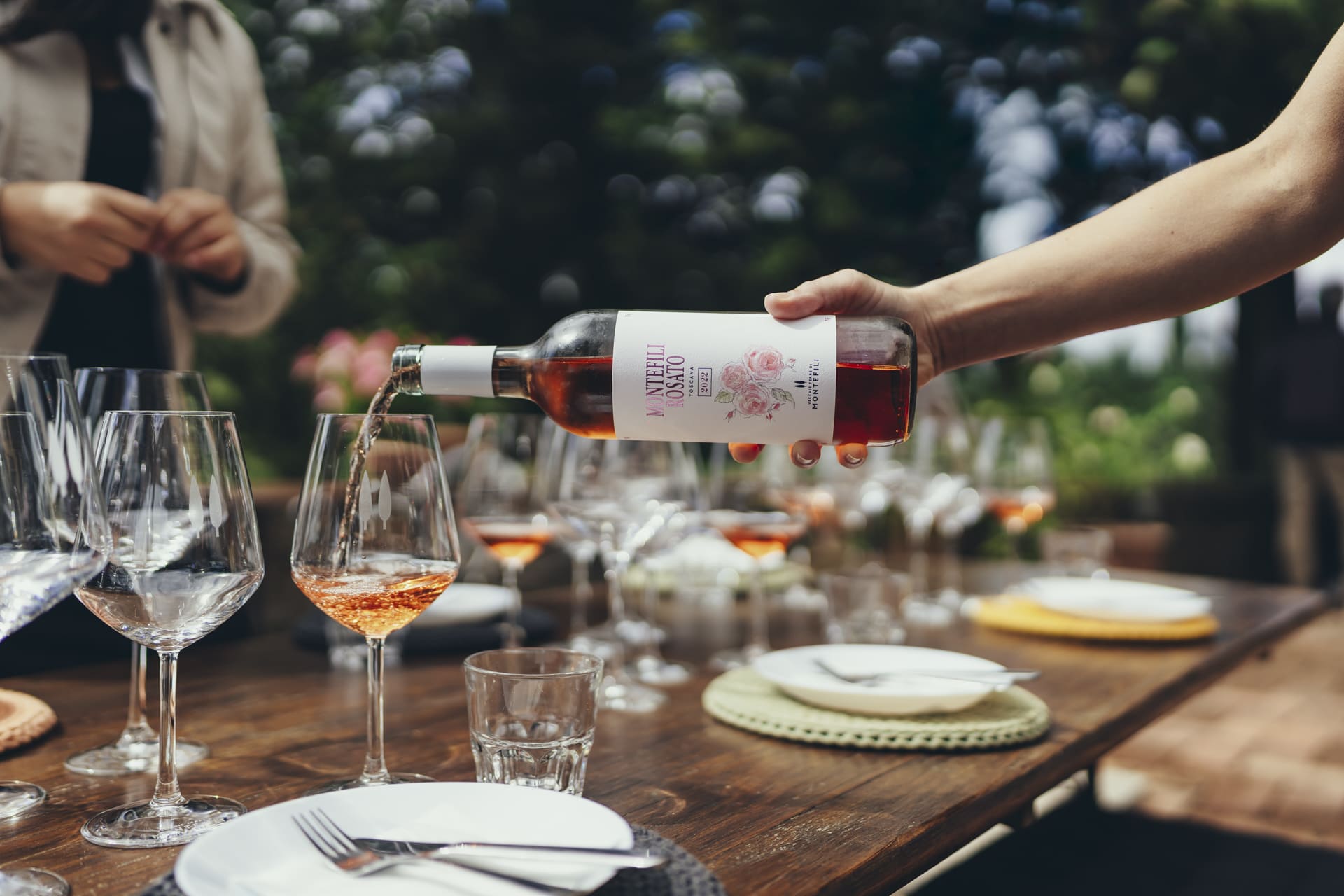 A host pours Montefili rosé into tasting glasses on an outdoor table