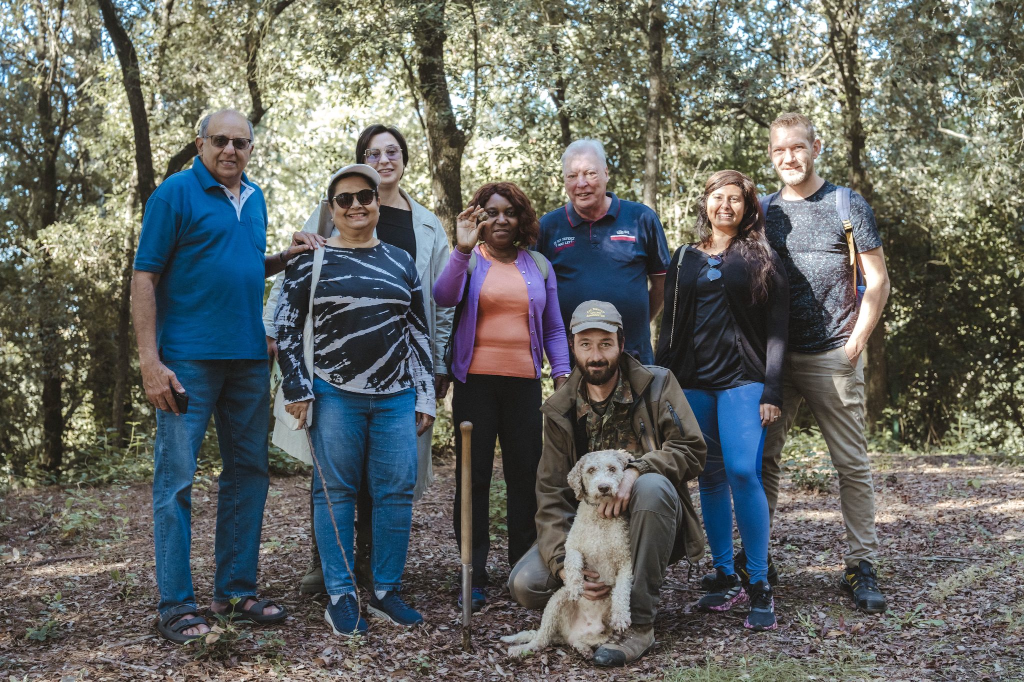 A group of guests poses in the woods with the truffle hunter and his dog after a truffle hunt