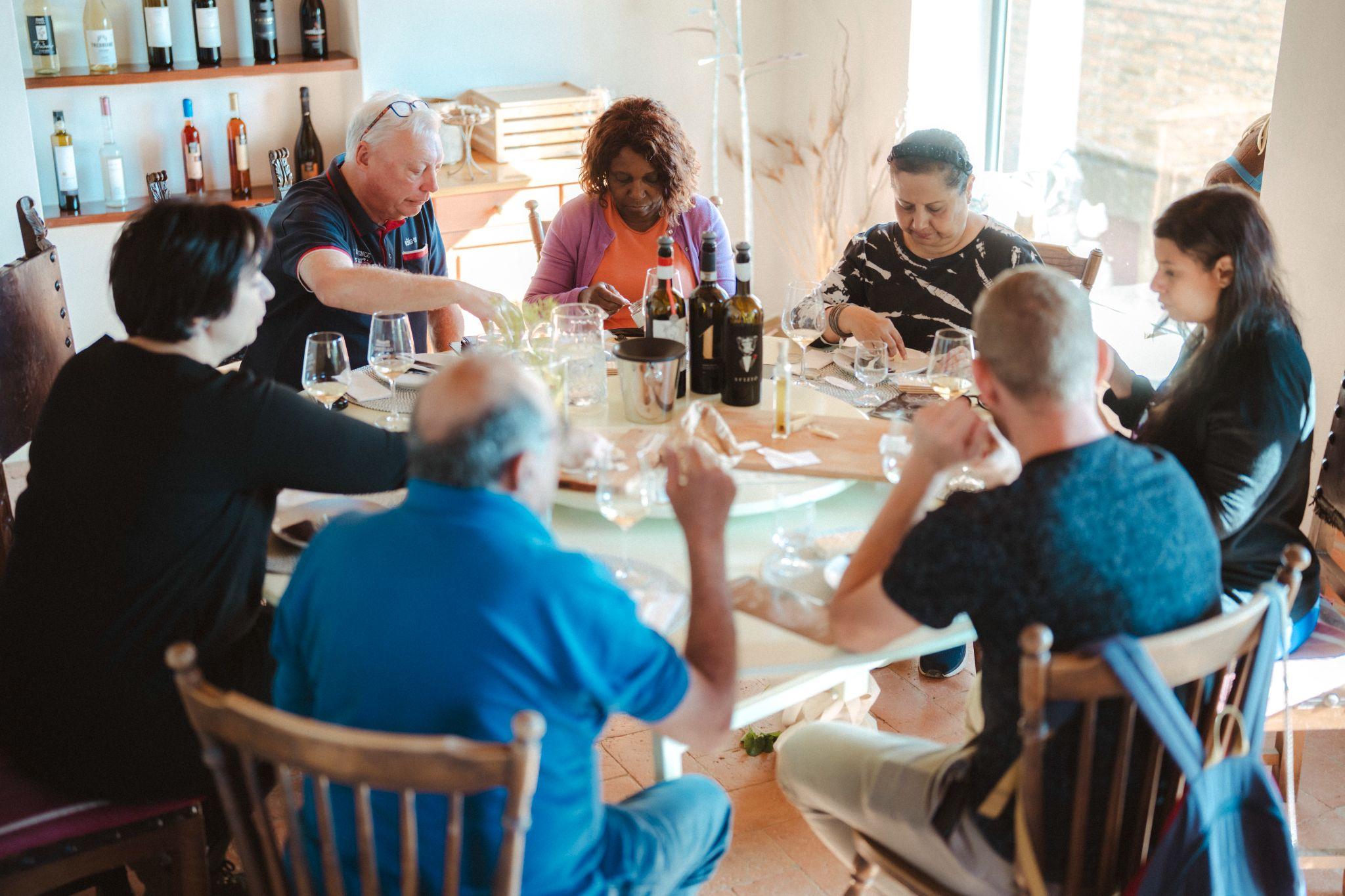 Guests seated around a round table with glasses of white wine and bottles in a bright dining room