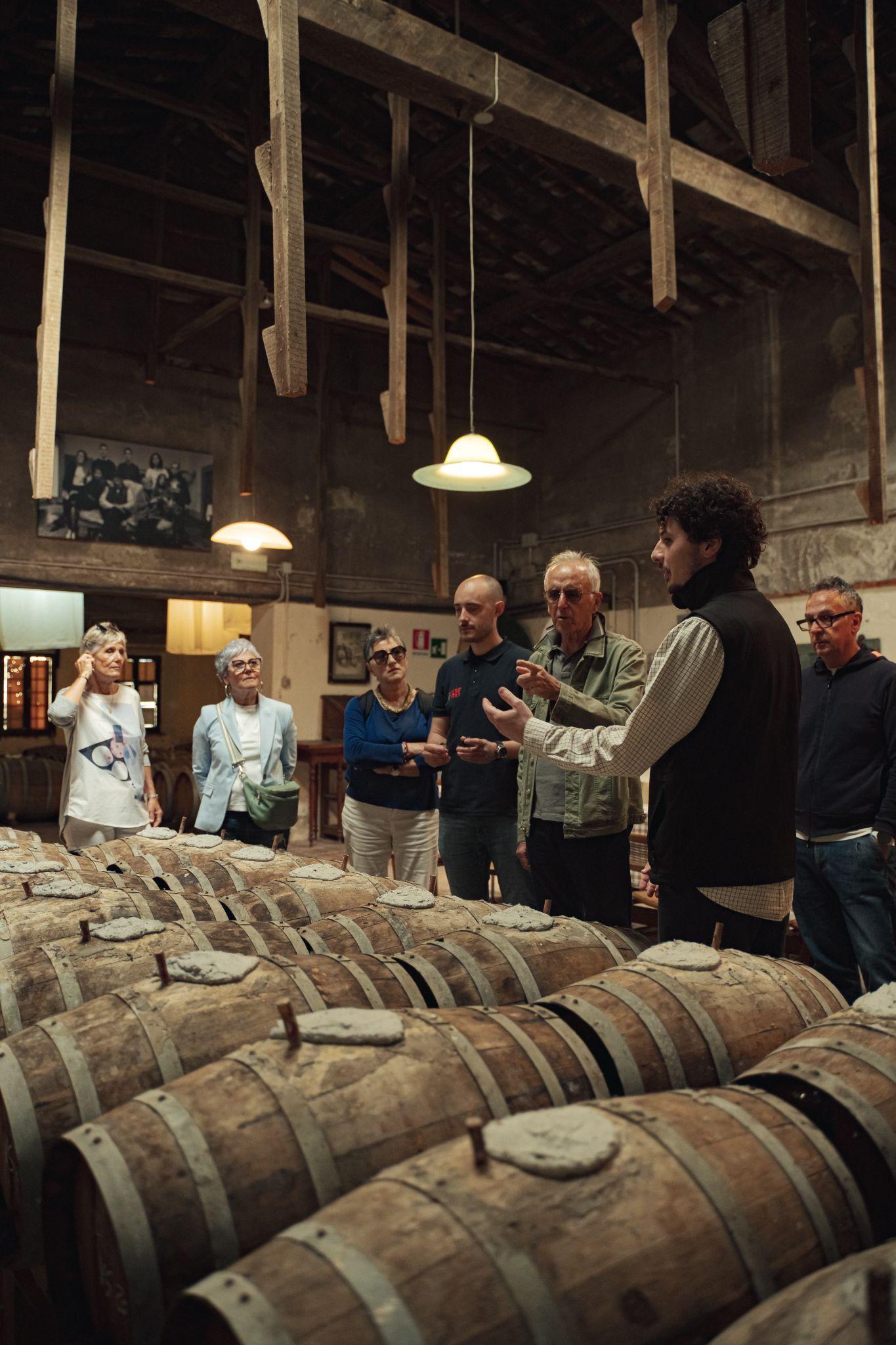 Guide talking to a small group among rows of old sealed barrels in a historic wine cellar with wooden beams